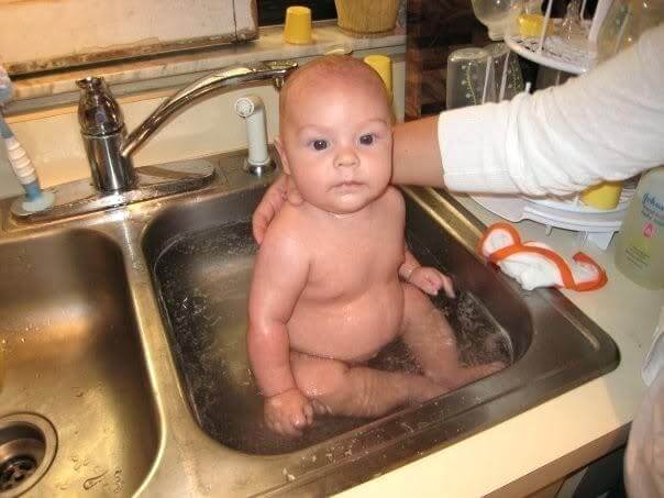 A baby being washed in the same sink as raw chicken.